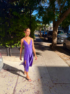 Woman wearing a purple lace slit midi dress on a sunny sidewalk