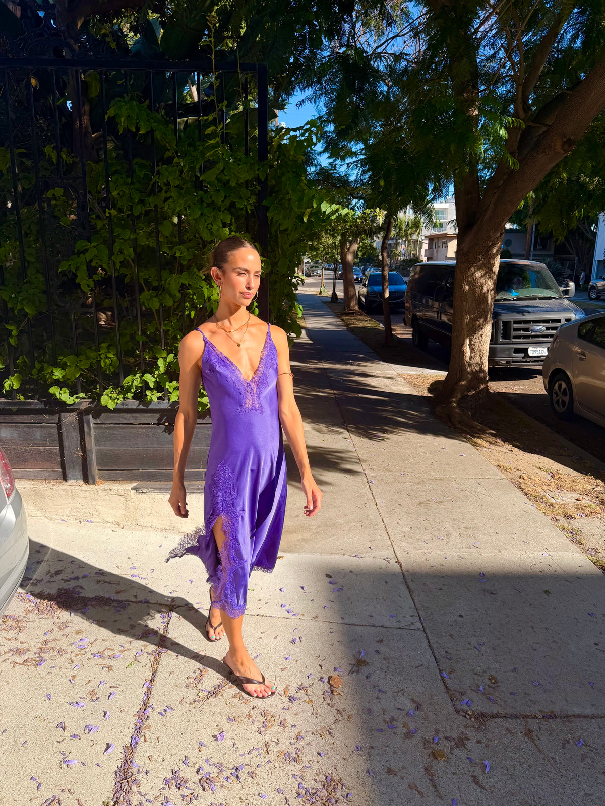 Woman wearing a purple lace slit midi dress on a sunny sidewalk