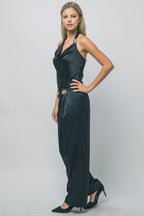 Woman wearing silky black trousers with gold hardware and matching halter top in a studio setting