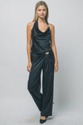 Woman wearing sleek black silky trousers with gold hardware and matching halter top in a studio setting