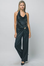 Woman wearing sleek black silky trousers with gold hardware and matching halter top in a studio setting