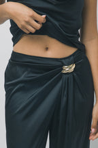 Close-up of silky black women's trousers with gold hardware detail and draped fabric at the waist.