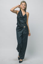 Woman modeling silky black trousers with gold hardware detail, paired with matching sleeveless top and black heels.