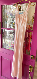 Vintage pale pink sleeveless slip dress with square neckline, lace trim, and small blue bow detail hanging on door.