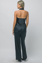 Woman wearing black silky trousers with gold hardware, styled with a matching black halter top from behind view