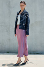 Woman wearing a pink satin midi skirt with a floral denim jacket and pointed heels