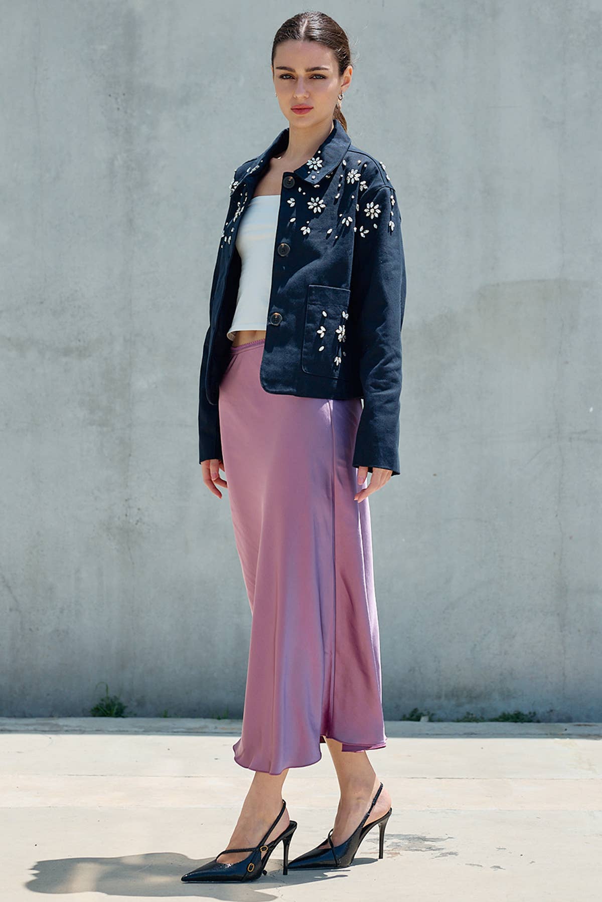 Woman wearing a pink satin midi skirt with a floral denim jacket and pointed heels