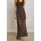 Woman wearing a black maxi skirt with white polka dots and a sheer chiffon fabric paired with a black sleeveless top.