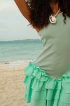Woman wearing a sleeveless ribbed top and mint green ruffled mini skirt on a sandy beach with ocean background