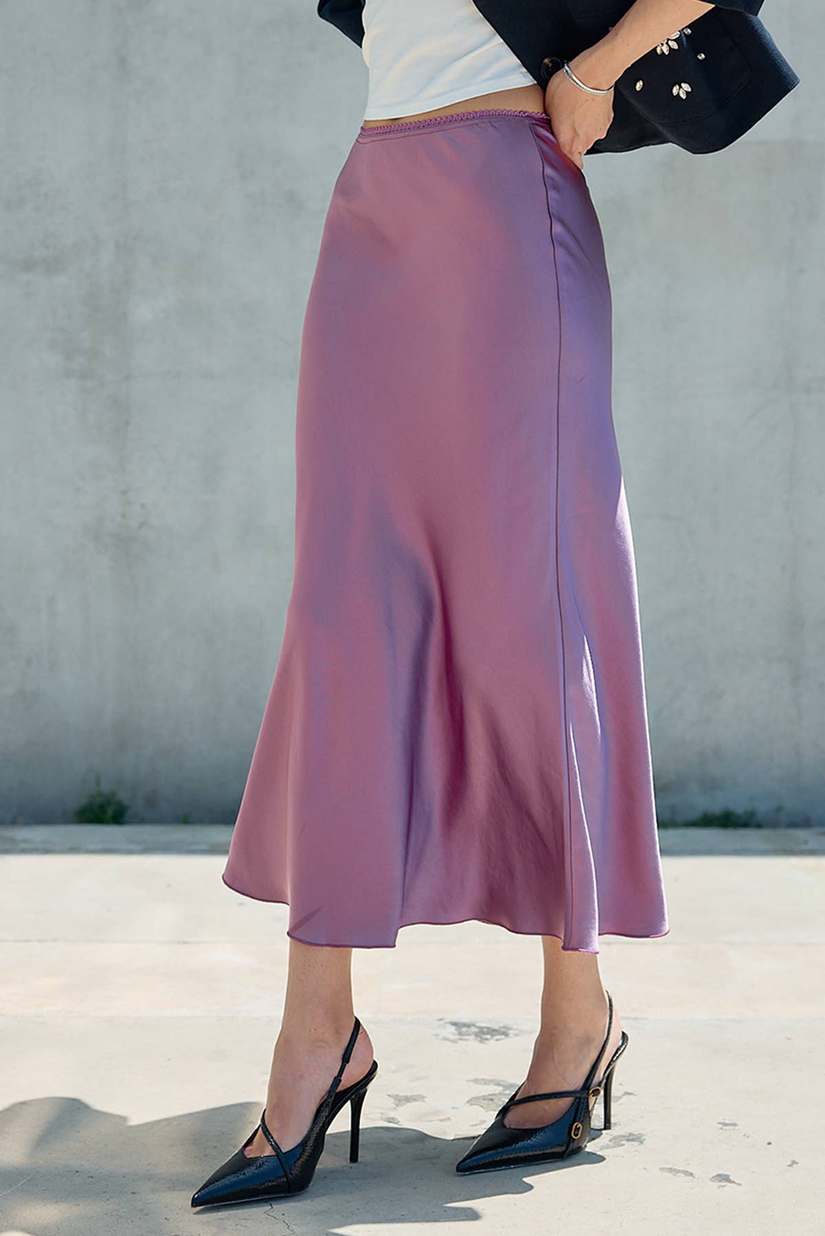 Woman wearing a mauve satin midi skirt with a flowing hem and black pointed heels