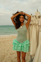 Woman in sleeveless ribbed dress with ruffled mini skirt standing on beach near folded umbrellas