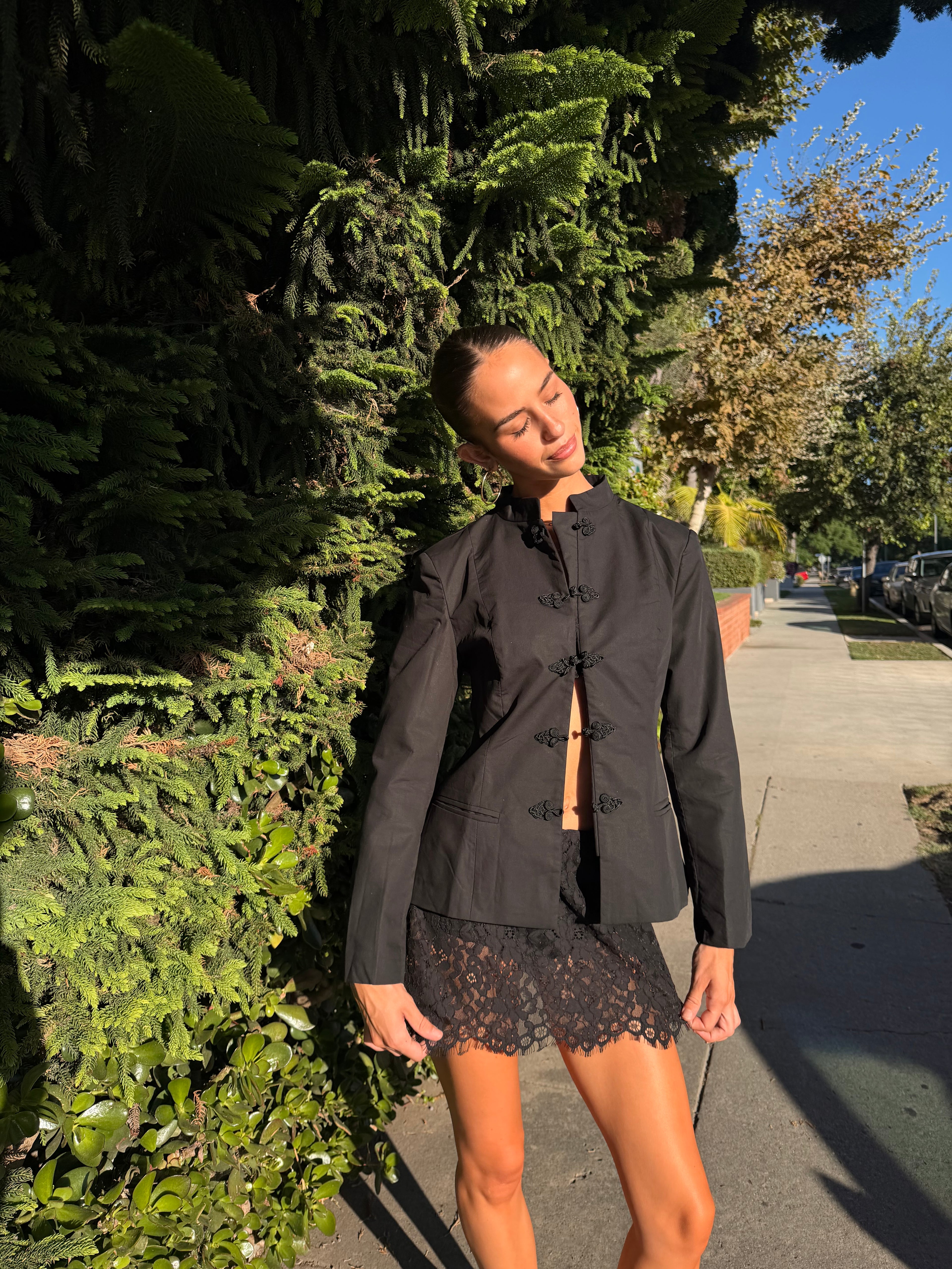 Woman wearing a black mandarin collar jacket with frog clasps outdoors