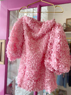 Pink women's mini dress with 3D floral texture and puff sleeves hanging on a gold hanger