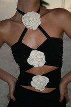Woman wearing a black mini dress with cream crochet rose cutout details and adjustable neck straps at sunset outdoors