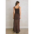 Woman wearing a brown polka dot maxi skirt with a black sleeveless top, viewed from the back against a neutral background.