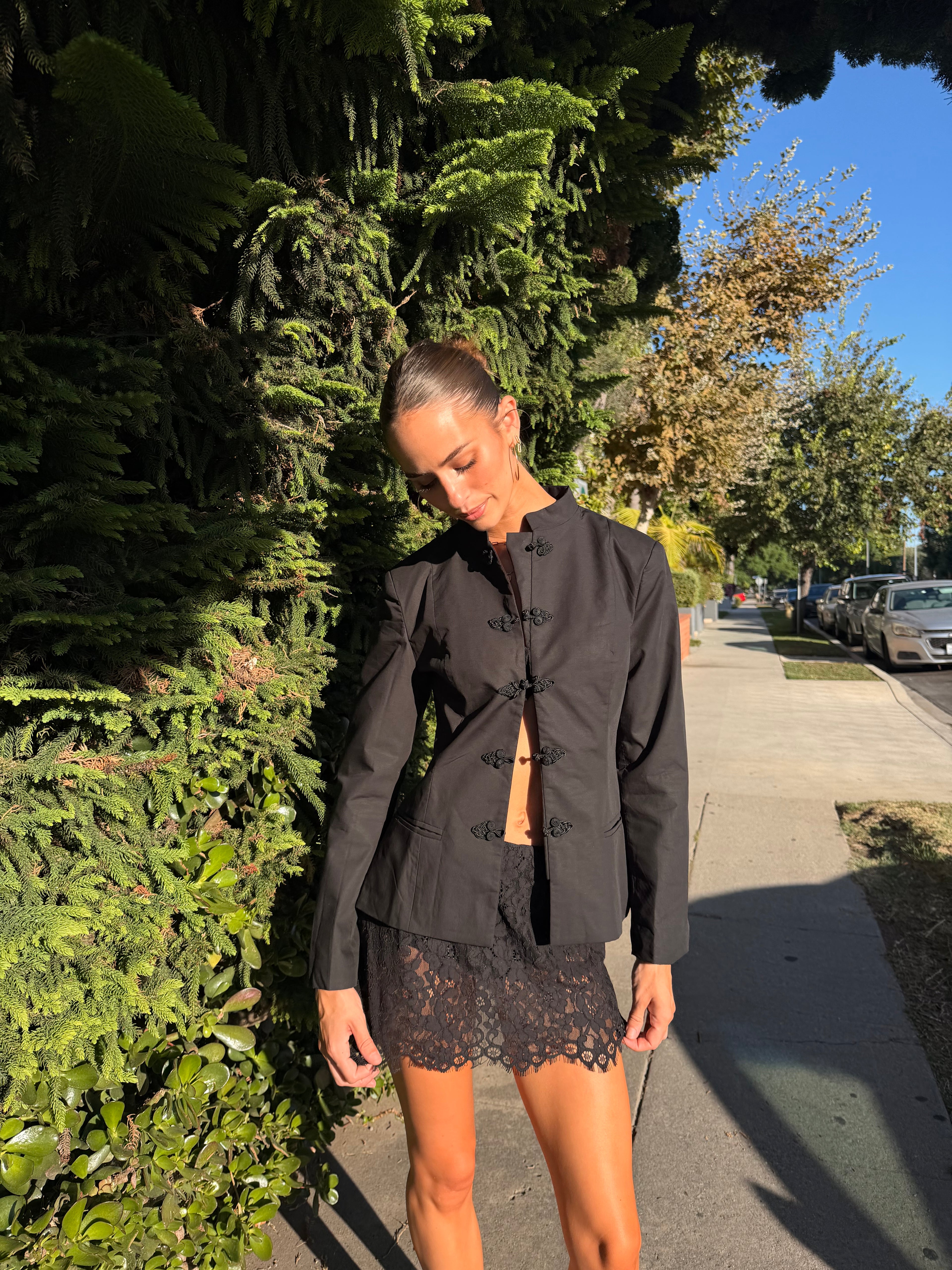 Woman wearing a black mandarin collar jacket with frog clasps and lace shorts outdoors