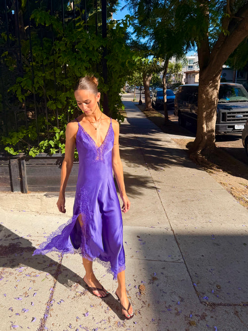 Woman wearing a purple satin lace slit midi dress on a sunny sidewalk