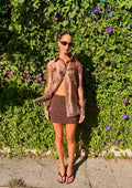 Woman wearing a sheer brown oversized button down blouse and patterned mini skirt outdoors