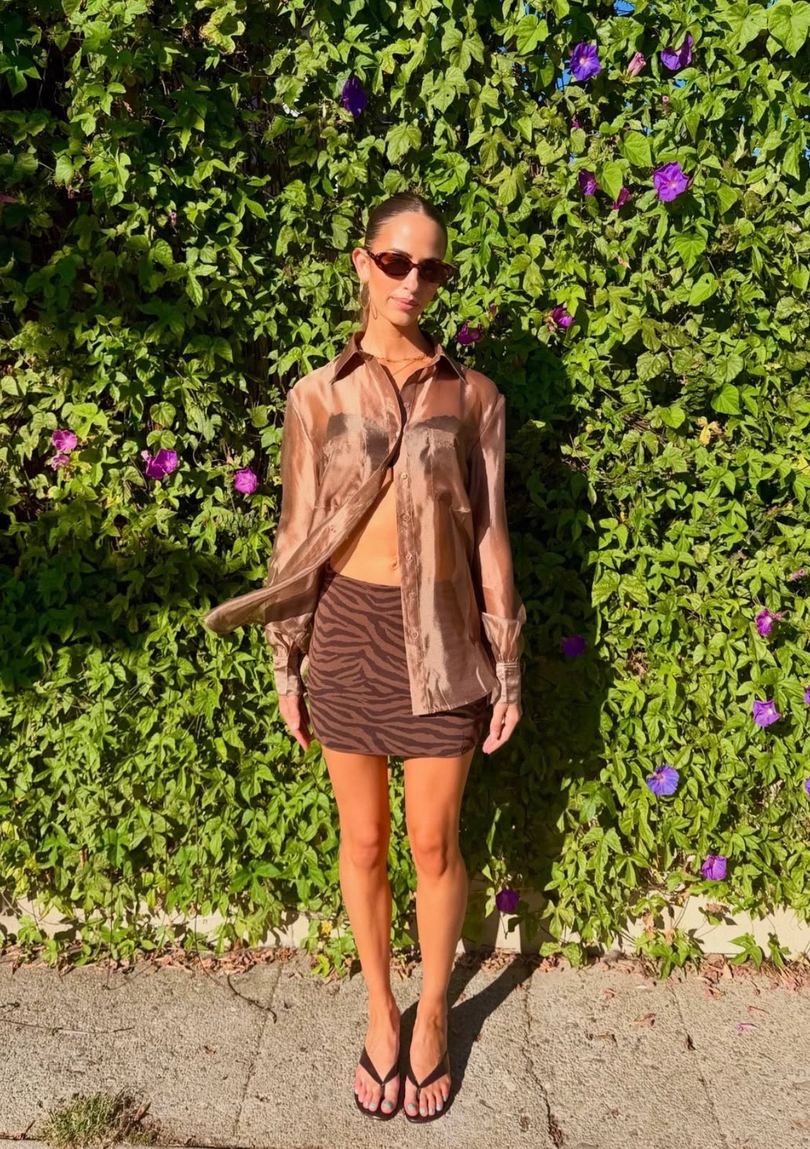 Woman wearing a sheer brown oversized button down blouse and patterned mini skirt outdoors