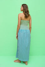 Woman wearing a strapless, smocked dress with a green checked top and blue striped midi skirt against a green wall.