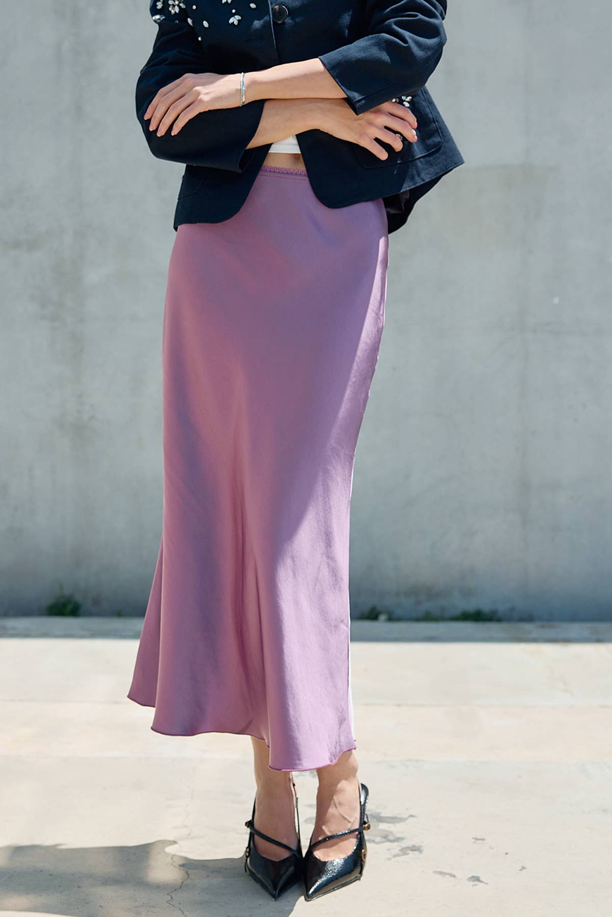 Woman wearing a lilac satin bias cut midi skirt with a black blazer and pointed heels