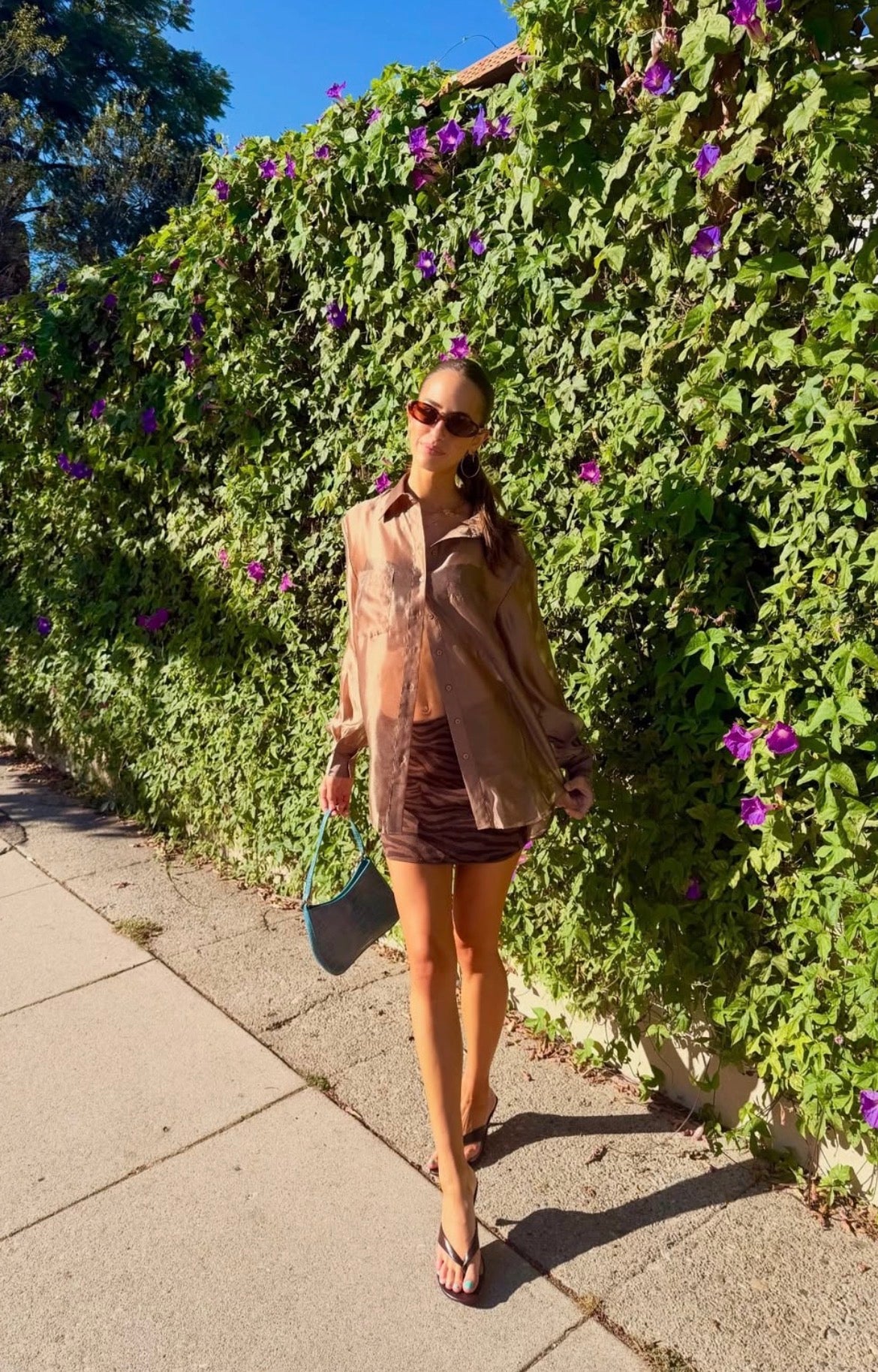 Woman wearing a sheer brown oversized button down blouse and mini skirt outdoors
