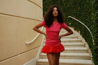 Woman in a fitted pink mini dress with a voluminous red hem standing on outdoor stairs in women's clothing style