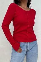 Woman wearing a fitted red cardigan with long sleeves and button front, paired with light blue jeans.