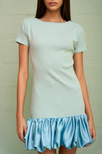 Woman wearing a fitted ribbed mini dress with a voluminous satin bubble hem in soft pastel colors