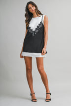 Woman wearing sleeveless black and white mini dress with lace detail and round neckline in studio setting