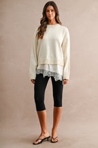 Woman wearing an ivory knit sweater with a layered satin hem and floral lace trim