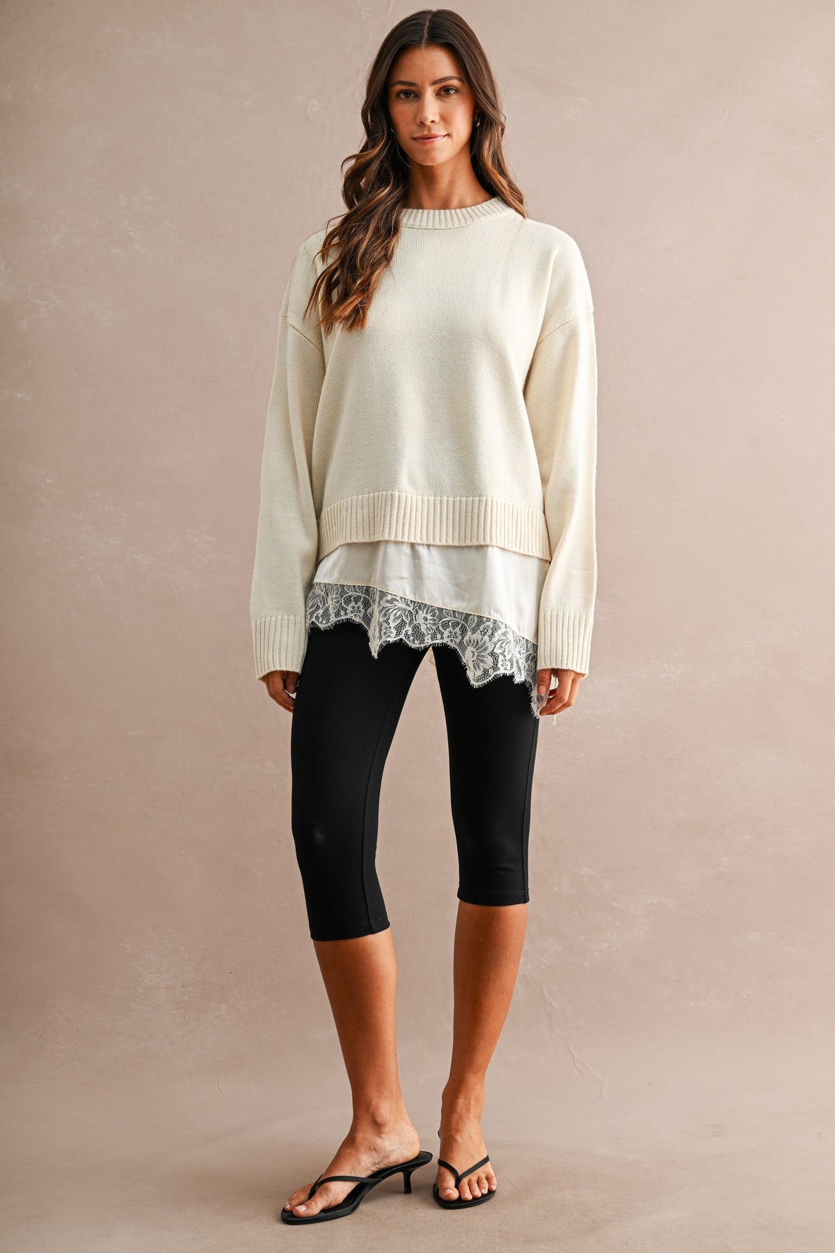 Woman wearing an ivory knit sweater with a layered satin hem and floral lace trim