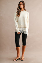 Woman wearing a cream knit sweater with lace trim hem and black leggings