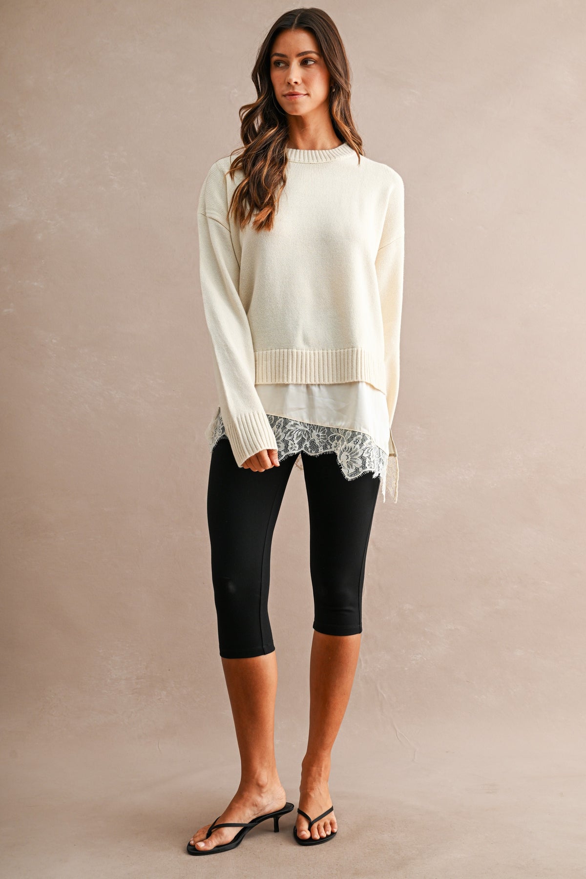 Woman wearing a cream knit sweater with lace trim hem and black leggings