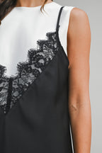 Close-up of a sleeveless women's mini dress with black lace overlay and white fabric background