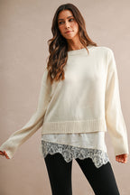 Women's cream knit sweater with ribbed trim and floral lace hem layered over black pants