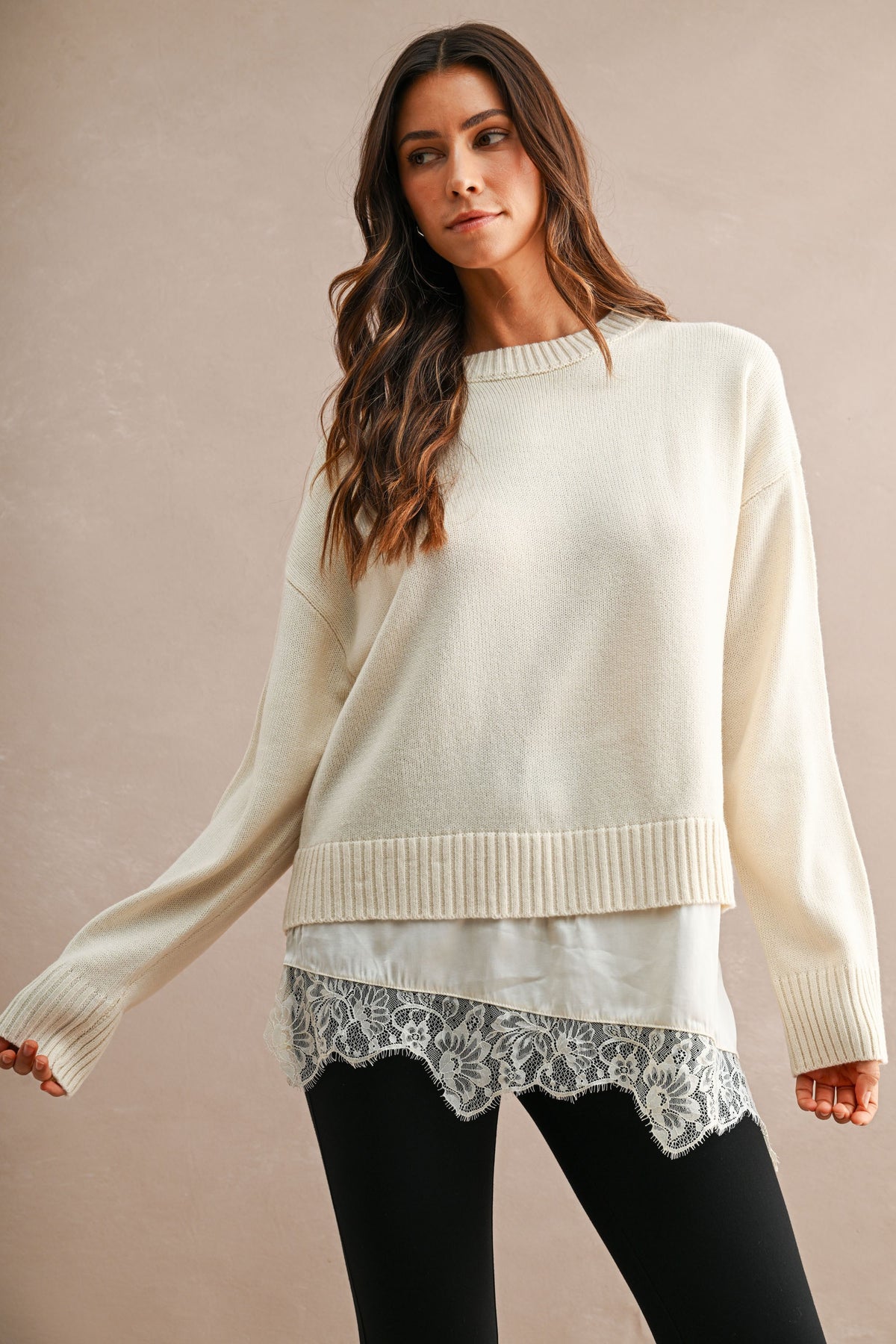 Women's cream knit sweater with ribbed trim and floral lace hem layered over black pants