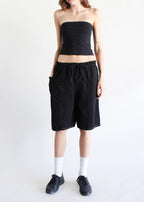 Woman wearing black elastic waist denim shorts paired with black tube top, white socks, and black shoes against white background