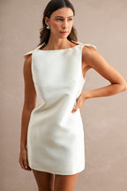Woman wearing sleeveless white mini dress with bow shoulder details and boat neckline in fashionable women's clothing.