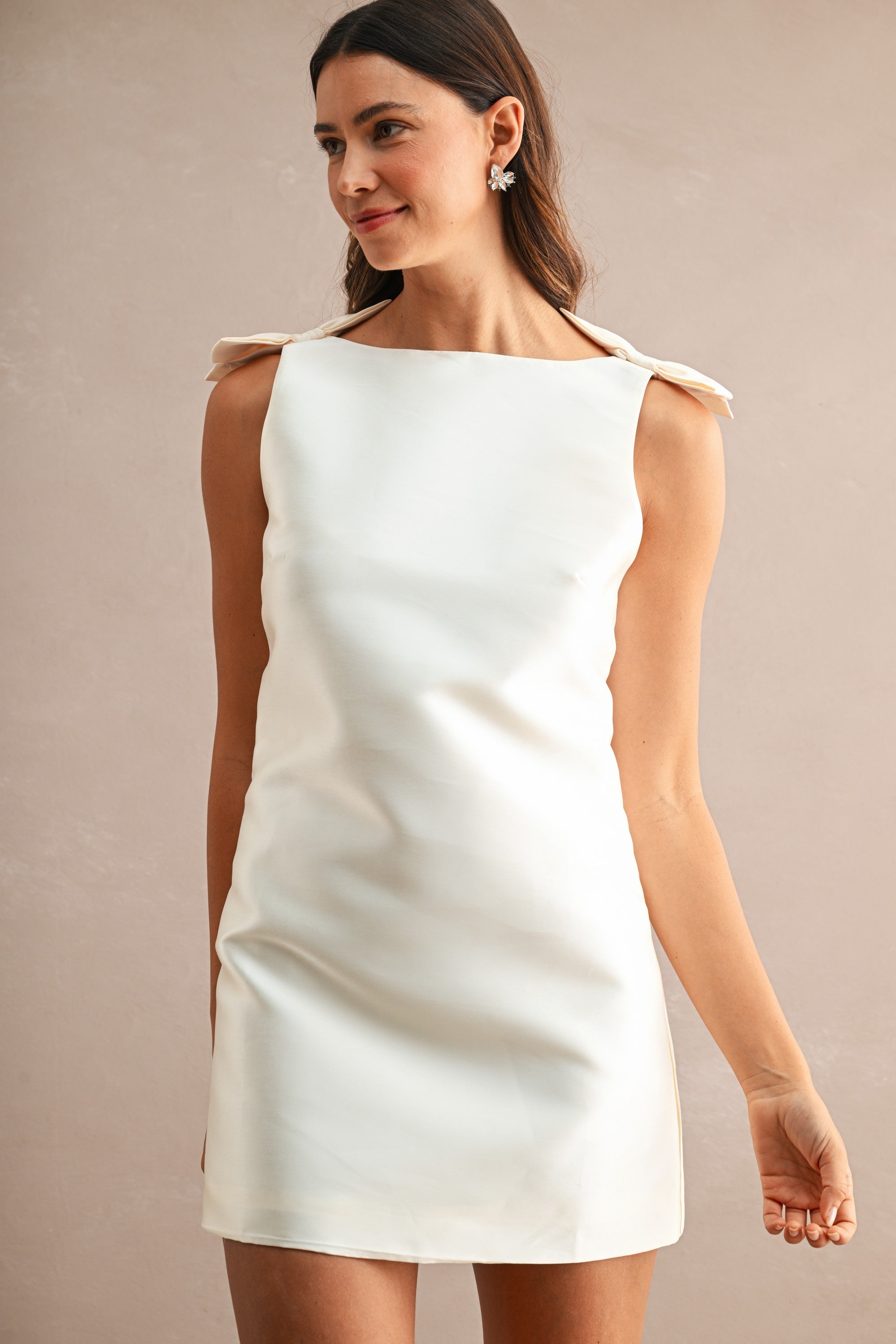 Woman wearing sleeveless white mini dress with boat neckline and bow details on shoulders in women's clothing.
