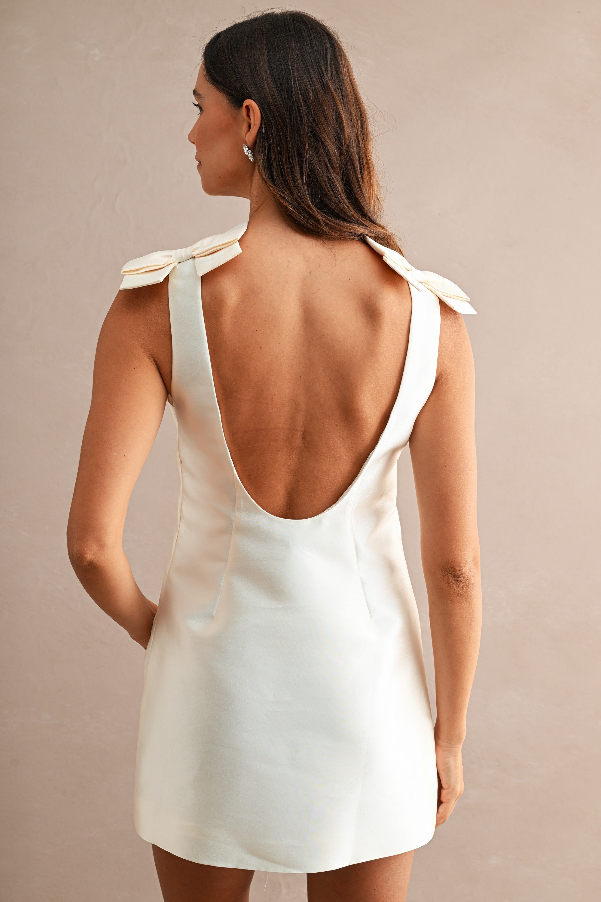 Woman wearing sleeveless mini dress with low scoop open back and bow details on shoulders in women's clothing.