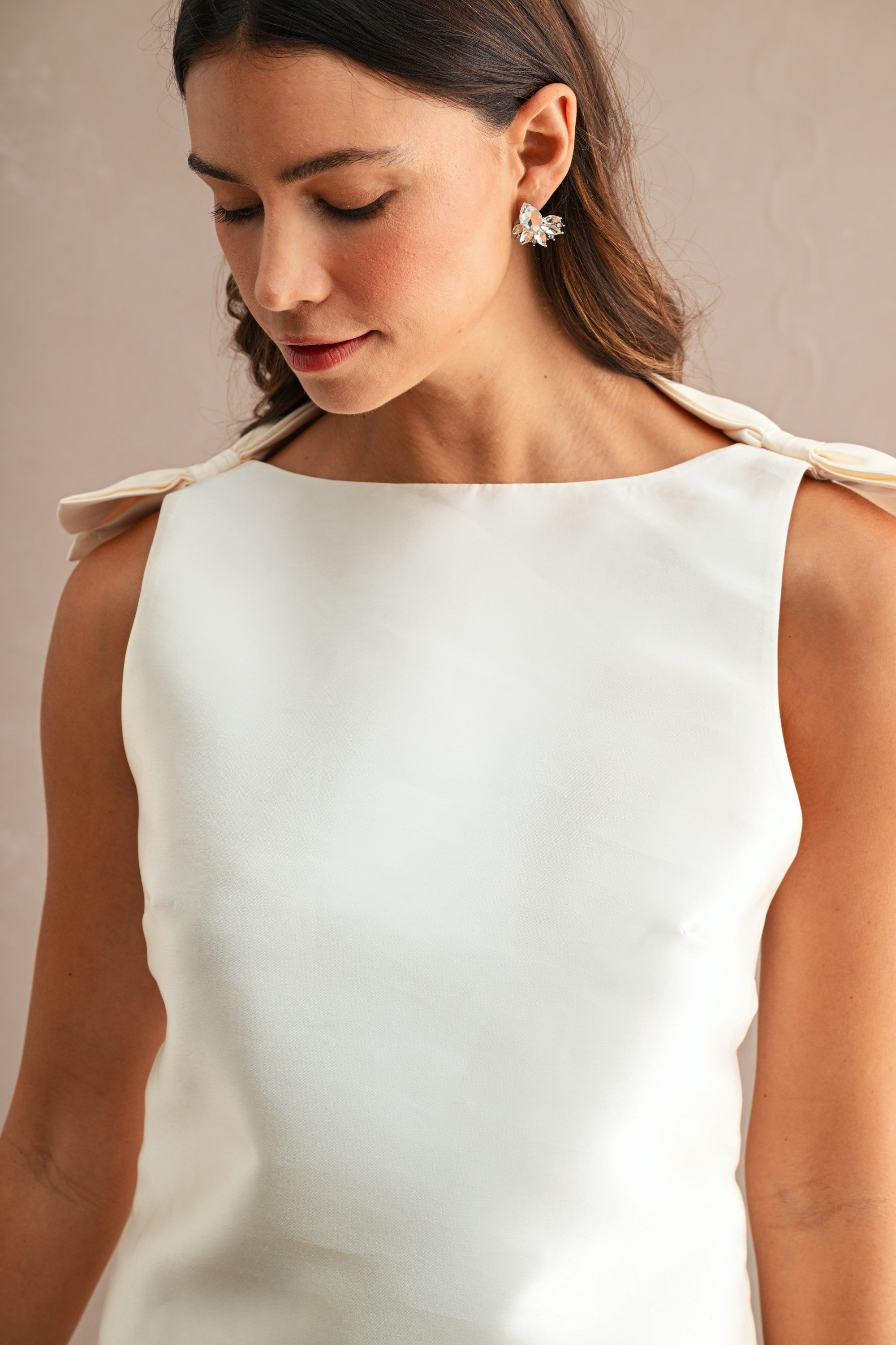 Close-up of woman wearing sleeveless white mini dress with boat neckline and bow shoulder details in women's clothing.