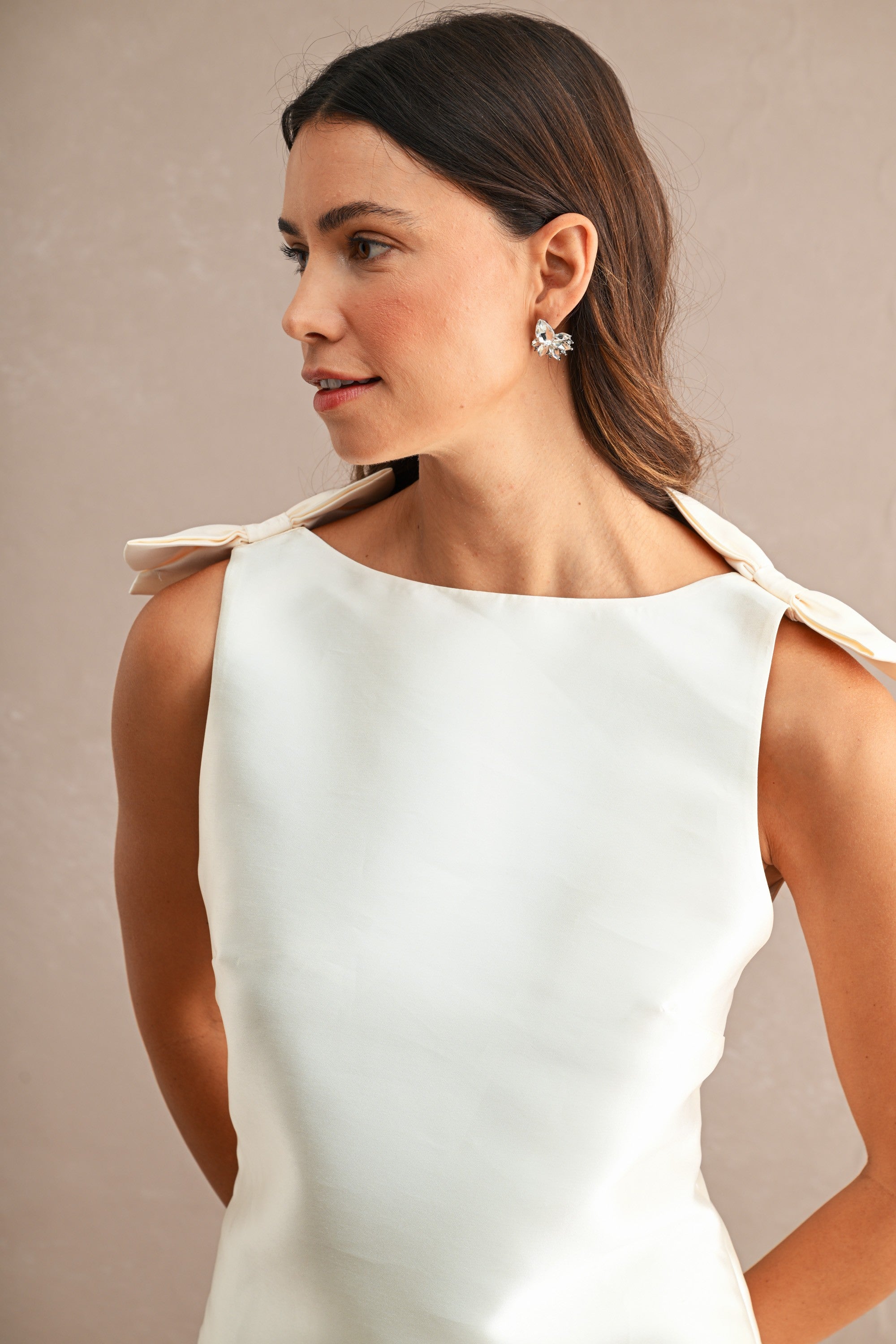 Woman wearing a sleeveless white mini dress with bow details on the shoulders and a boat neckline in women's clothing
