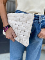 Hand holding a cream woven vegan leather clutch paired with casual white top and blue jeans.