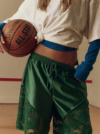 Womens clothing model wearing green satin shorts with lace panels and a cropped white top holding a basketball