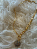 Gold chain necklace with a rhinestone encrusted heart pendant on a soft fabric background