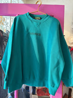 Teal oversized sweatshirt with STONER embroidery, vintage style, hanging on gold hanger in bright boutique setting
