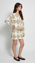 Woman wearing beige and white argyle knit cardigan and matching skort with black flats in studio setting