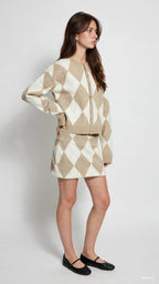 Woman wearing beige and white argyle knit cardigan and matching skort with black flats in studio setting