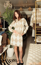 Woman modeling beige and white argyle knit cardigan and matching mini skort in a stylish boutique setting